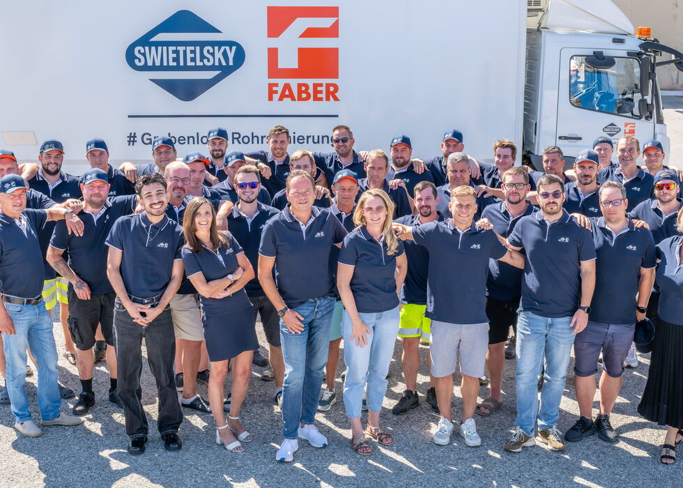 Große Gruppe von Mitarbeitenden posiert gemeinsam vor einem beschrifteten Lkw an einem sonnigen Tag.