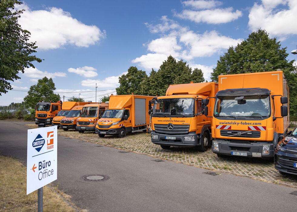 Eine Reihe orangefarbener Lieferwagen und Lkw steht neben einem Schild für Büro Office an einem sonnigen Tag.