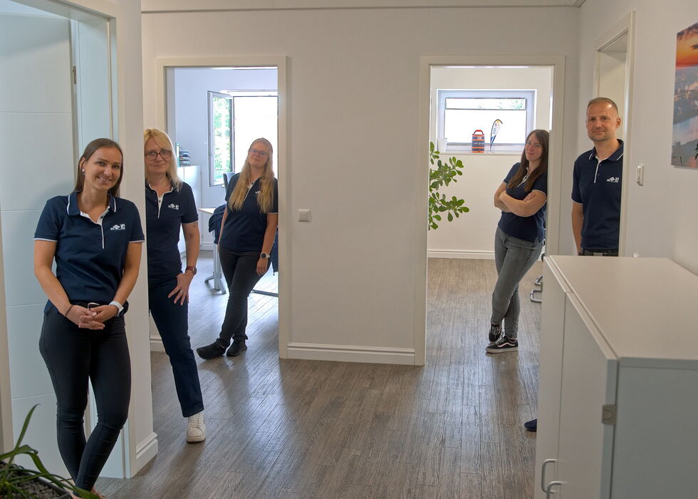 Four employees standing in a bright office hallway, posing between two doorways.