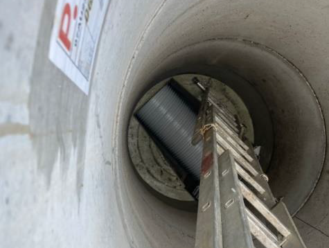 Blick in ein Betonrohr mit einer Leiter, die zu einem Arbeiter oder Gerät darunter führt.