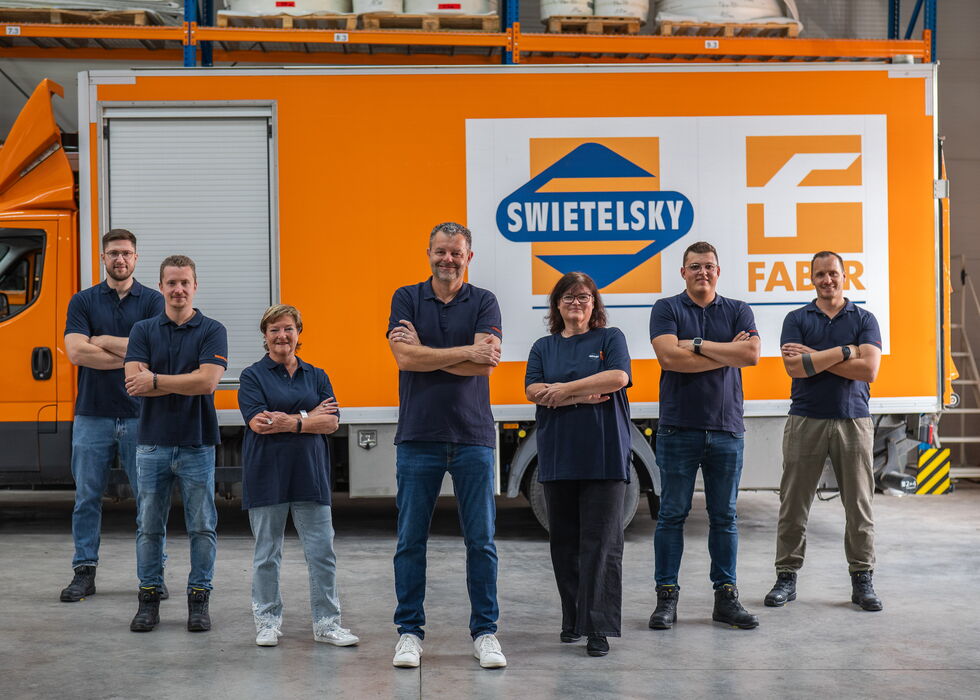 Sechs Mitarbeitende stehen vor einem orangefarbenen SWIETELSKY- und Faber-Lkw in einer Werkstatt.