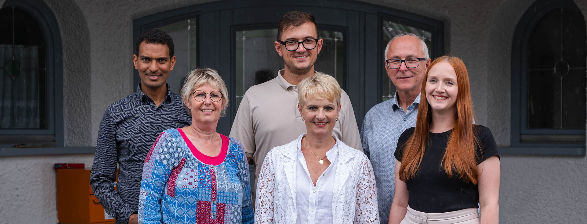 Sechs Personen stehen gemeinsam für ein Gruppenporträt vor einem Gebäude.