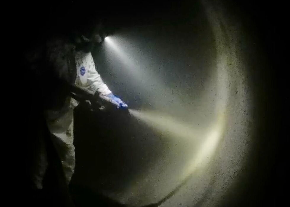 Ein Arbeiter in Schutzkleidung sprüht Flüssigkeit in einem dunklen Tunnel, beleuchtet von einem hellen Strahl.