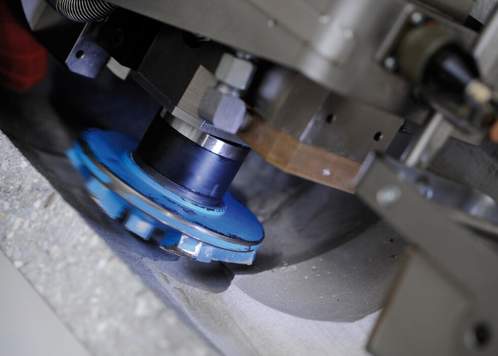Nahaufnahme einer Schleifscheibe, die eine Metalloberfläche in einer Industriemaschine bearbeitet.