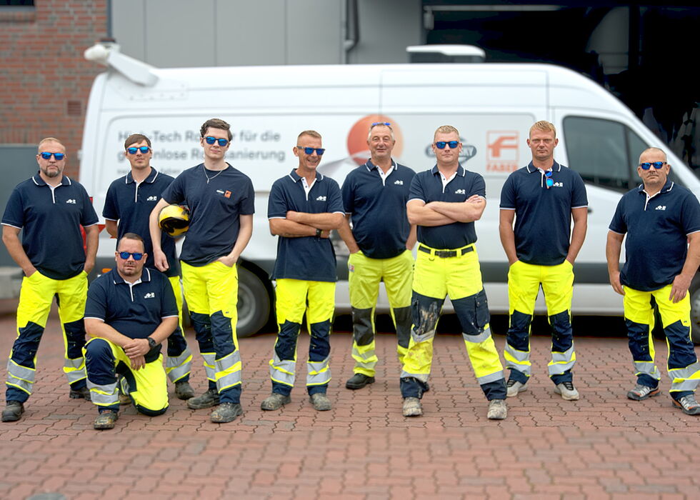 Eight workers posing in front of a white van, wearing navy shirts and bright yellow high-visibility trousers.